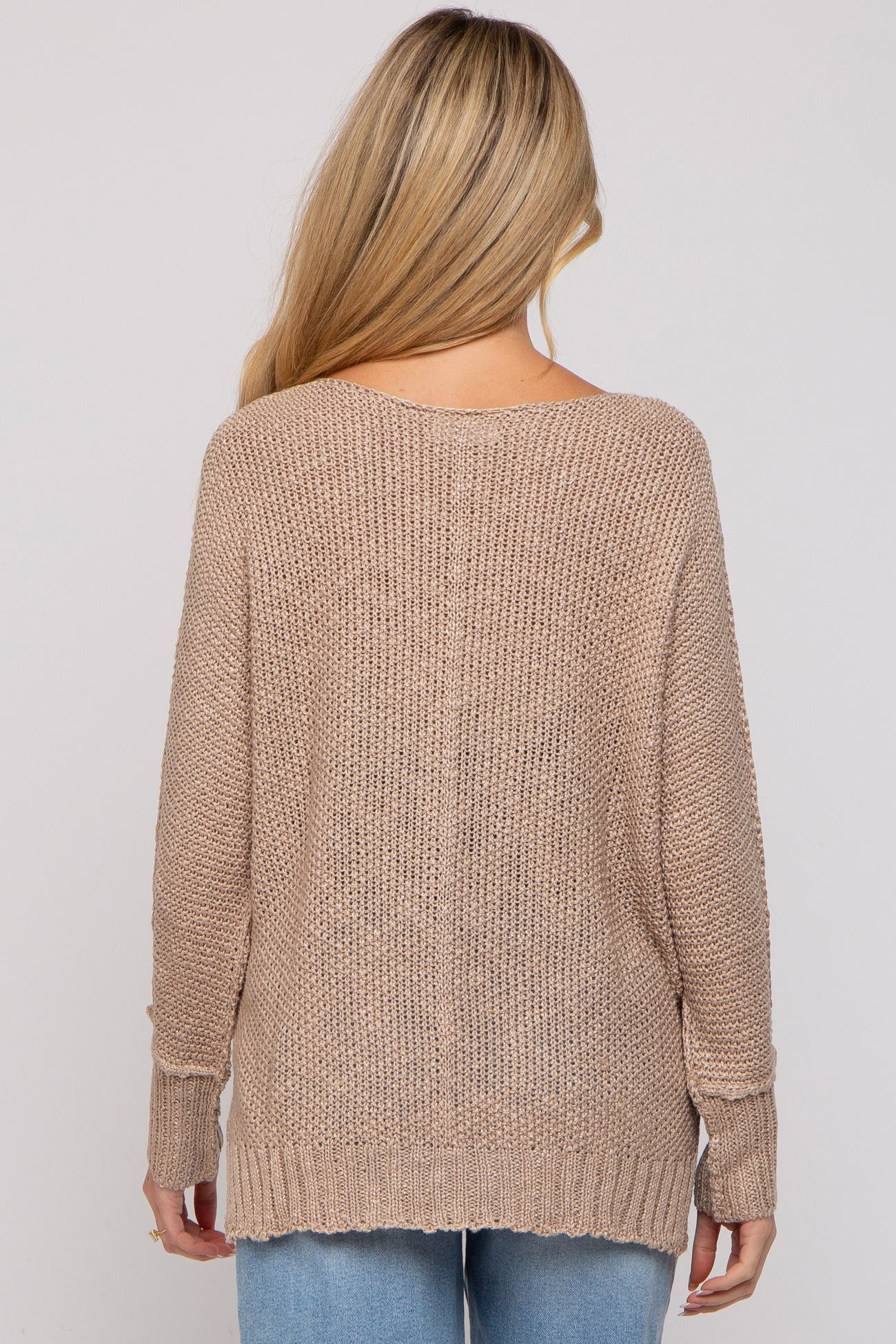 woman wearing a beige loosely knit maternity sweater with long sleeves, viewed from the back
