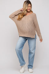 woman wearing a beige oversized maternity sweater and blue distressed jeans, with a baby bump visible