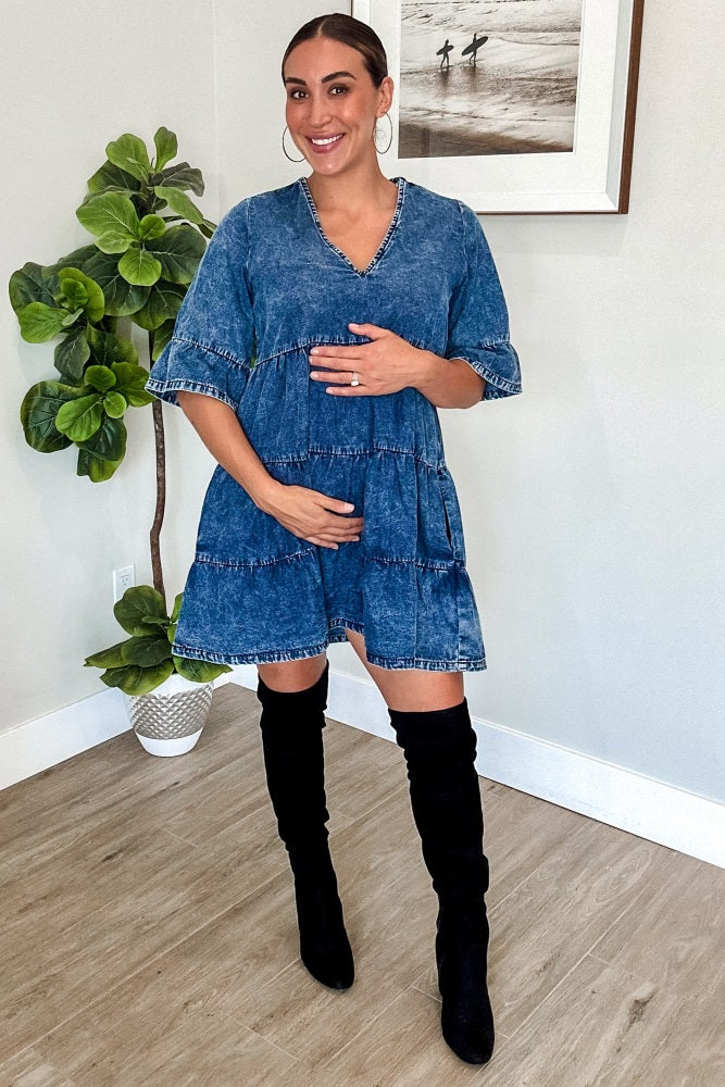 woman wearing a denim tiered maternity dress and holding her baby bump