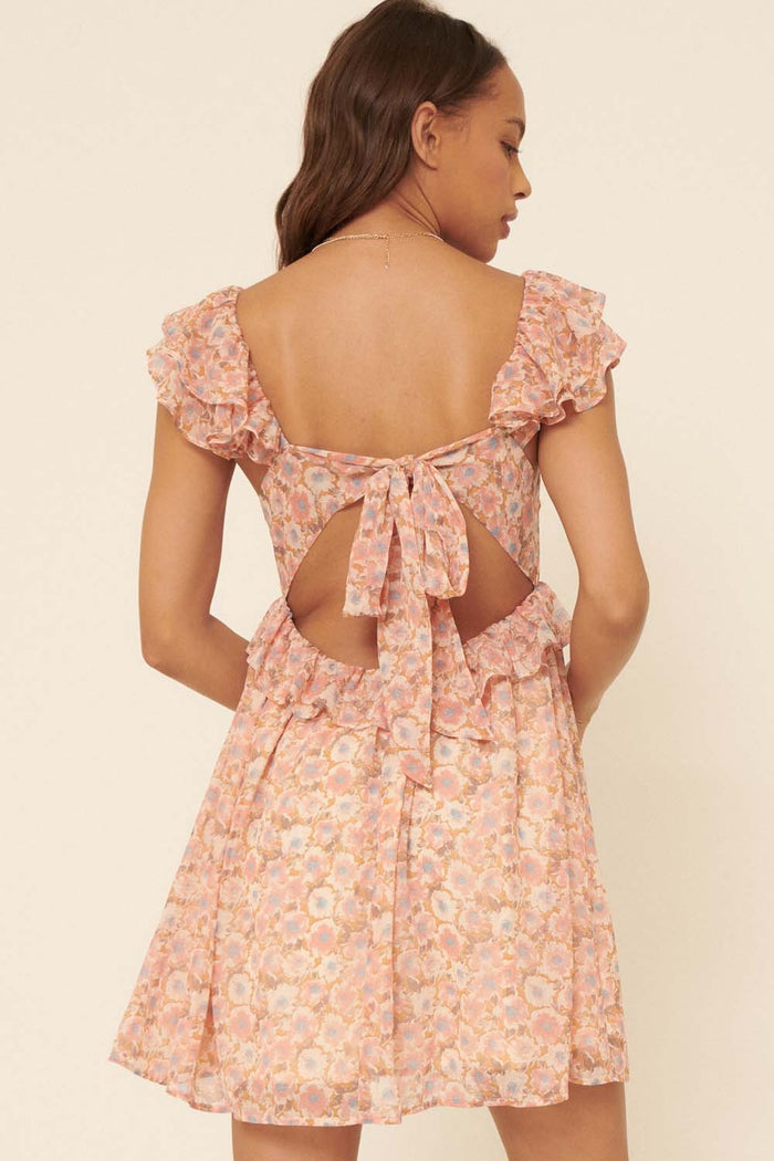 woman wearing a pink floral dress with ruffle sleeves and an open back featuring a tie detail