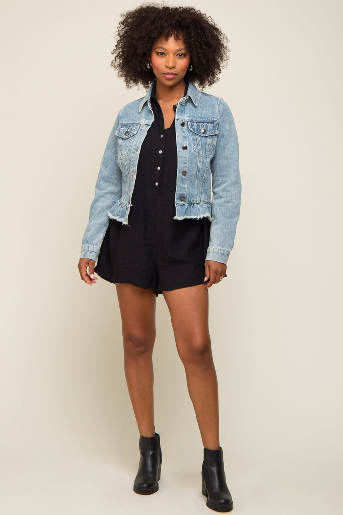 woman wearing a light wash denim jacket over a black romper with buttons and ankle boots