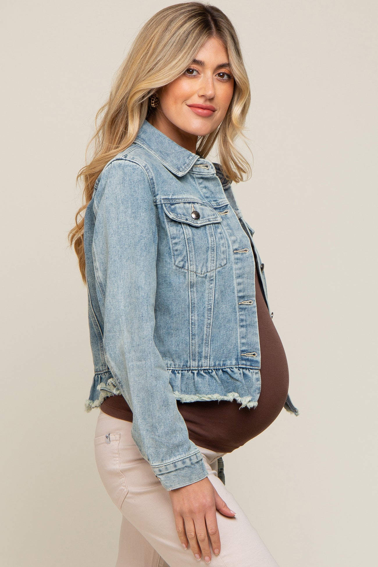 woman wearing a light wash maternity denim jacket over a brown top, showcasing her baby bump