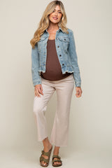 woman wearing a light blue denim jacket over a brown maternity tank top and cream maternity pants, visible baby bump