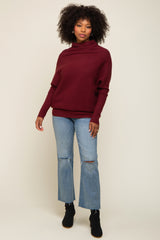 woman wearing a burgundy cozy sweater with a high neckline and light blue distressed flared jeans