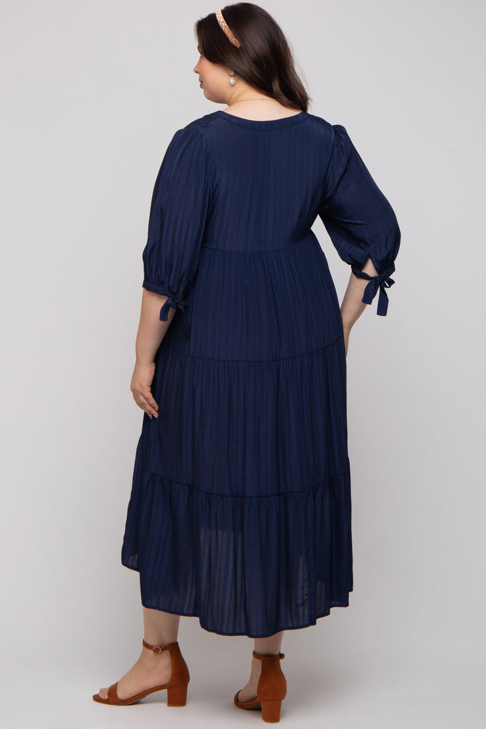 woman wearing a navy blue maternity plus-size tiered maxi dress with puff sleeves and adjustable bows at the cuffs