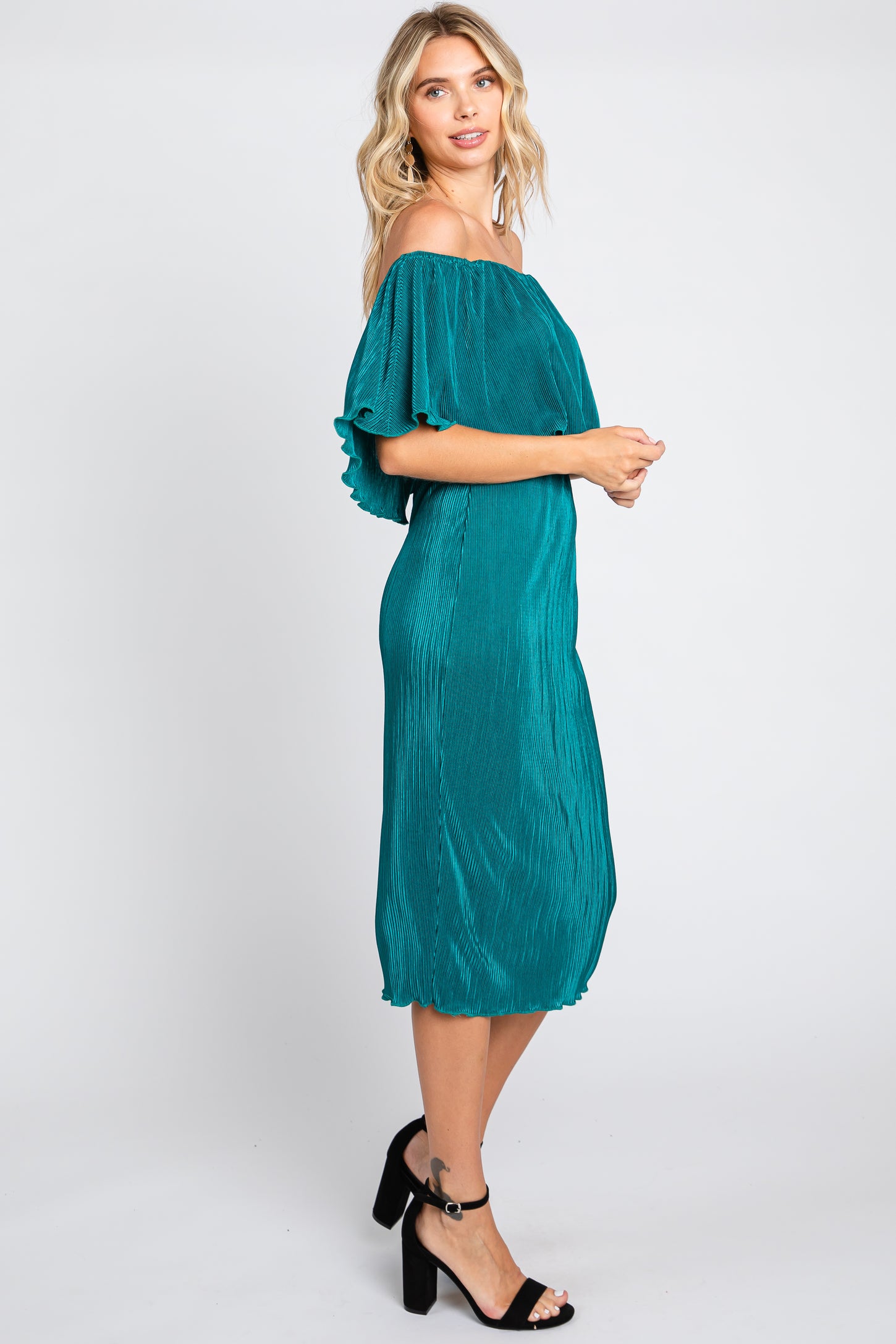 woman wearing a teal off-the-shoulder midi dress with ruffle sleeves and a pleated design, standing sideways
