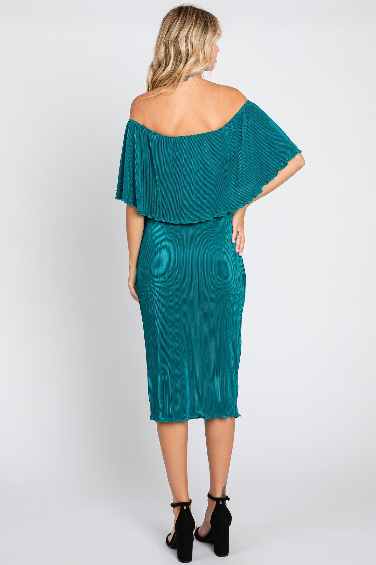woman wearing a teal off-the-shoulder pleated dress with a flowing cape style back and fitted silhouette