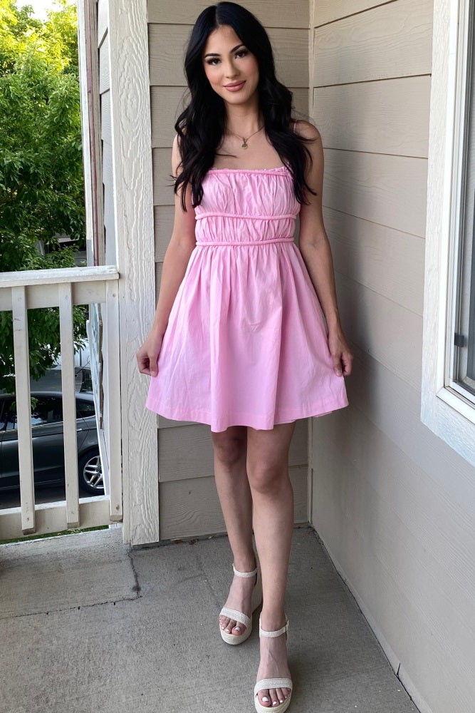 woman wearing a pink sleeveless babydoll dress and white platform sandals standing on a balcony