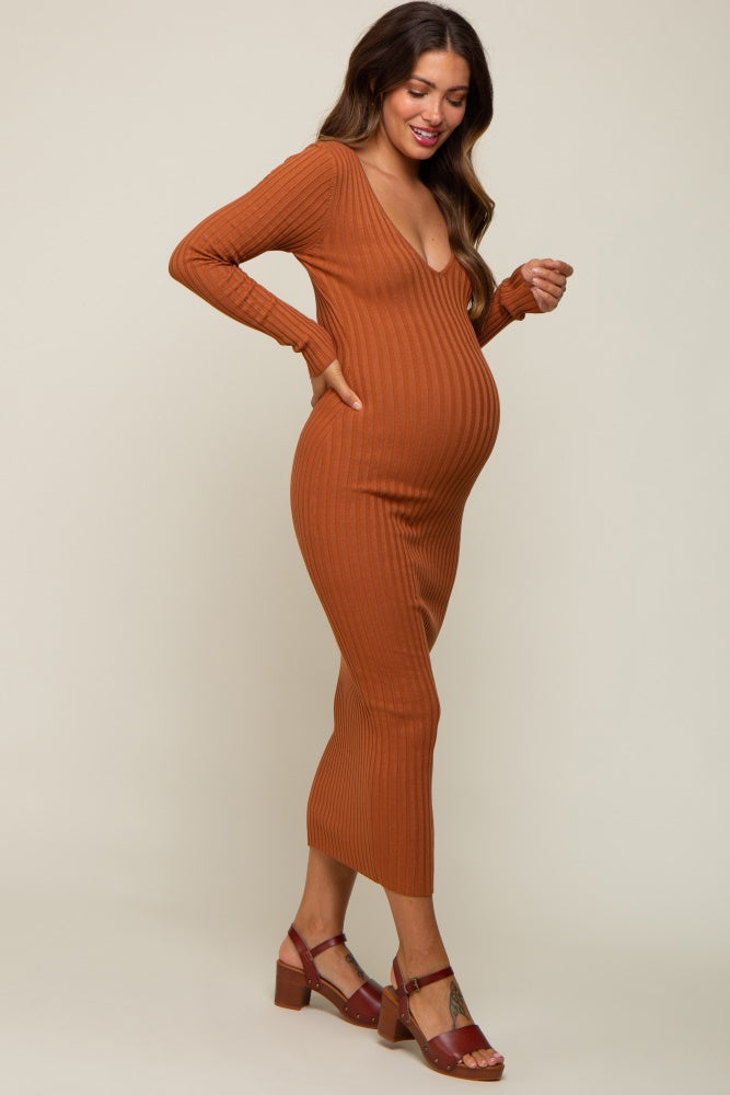 woman wearing a rust ribbed maternity dress with a plunging neckline and long sleeves, showing her baby bump