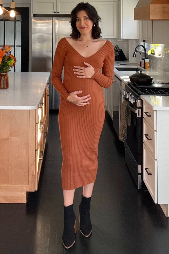 pregnant woman in a rust orange ribbed maternity midi dress and black ankle boots standing in a kitchen