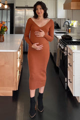 pregnant woman in a rust orange ribbed maternity midi dress and black ankle boots standing in a kitchen