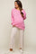 woman wearing a pink oversized maternity sweater and light beige flared pants, showing her baby bump