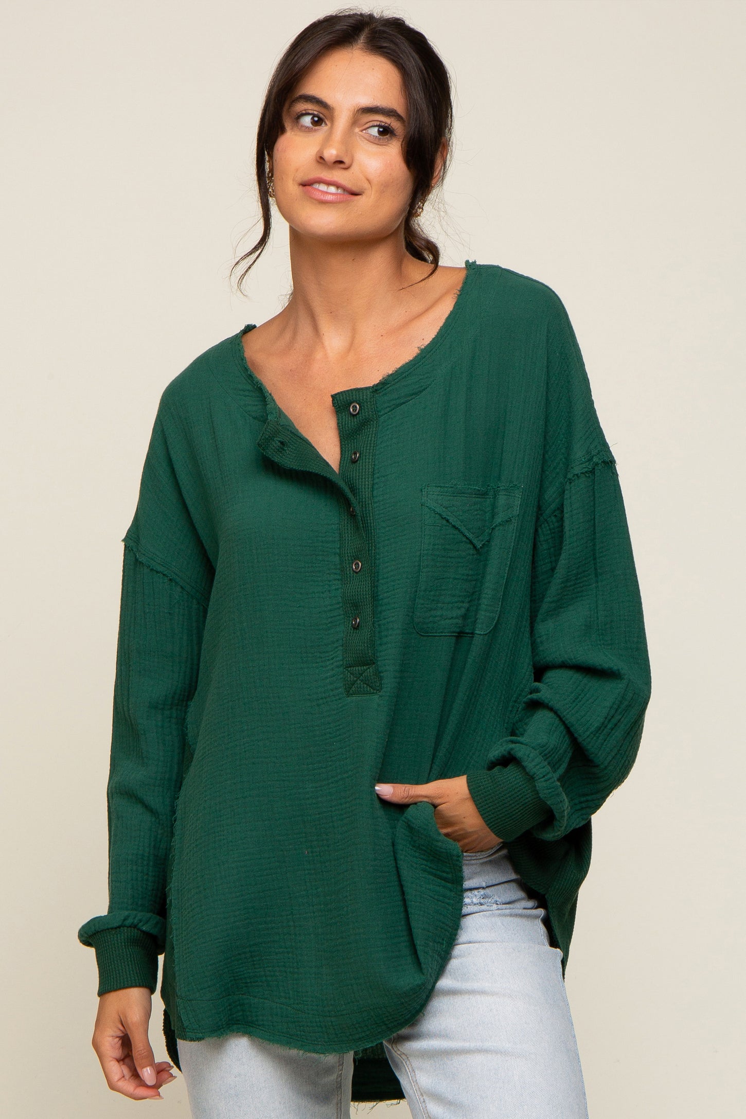 woman wearing a green oversized henley shirt with a pocket and button details, paired with light blue jeans
