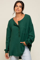 woman wearing a green oversized henley shirt with a pocket and button details, paired with light blue jeans