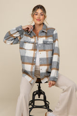 woman wearing a gray and white plaid maternity shirt jacket over a light top, sitting on a stool with a relaxed pose