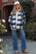 woman wearing a blue and cream checkered maternity shacket with pockets, paired with wide-leg jeans and a white cap