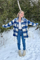 woman wearing a blue and white plaid shacket with a white top, light blue jeans, and cream-colored boots in a snowy setting