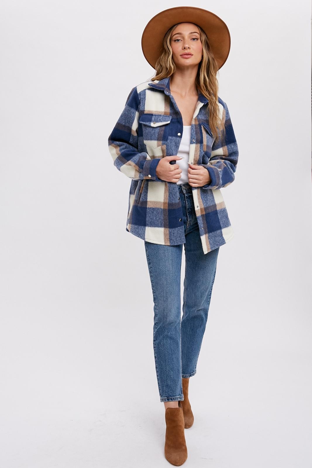 Woman wearing a blue and white plaid shacket with a brown wide-brim hat and blue jeans