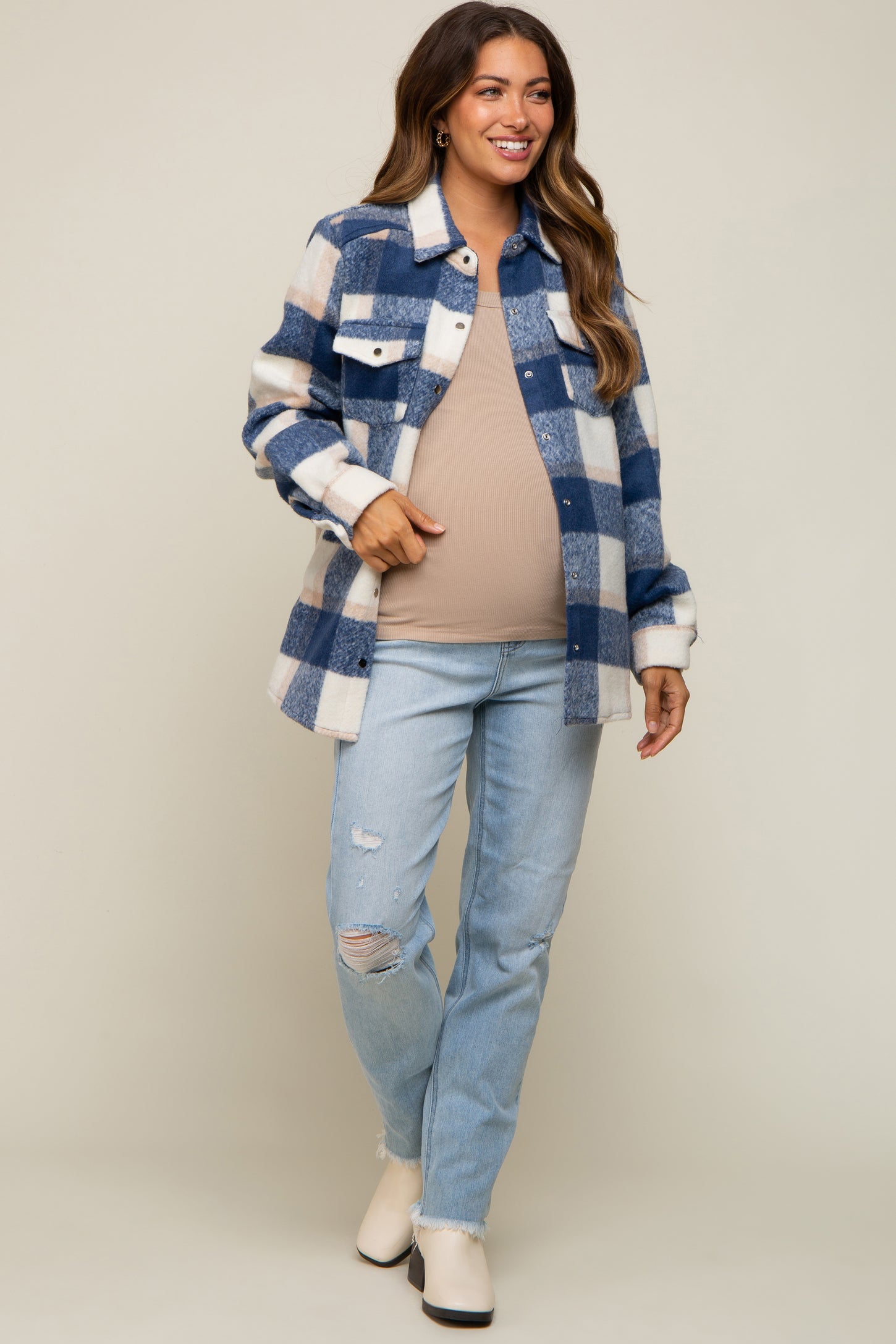 woman wearing a blue and white checkered maternity shirt jacket over a beige top and distressed jeans, showing her baby bump