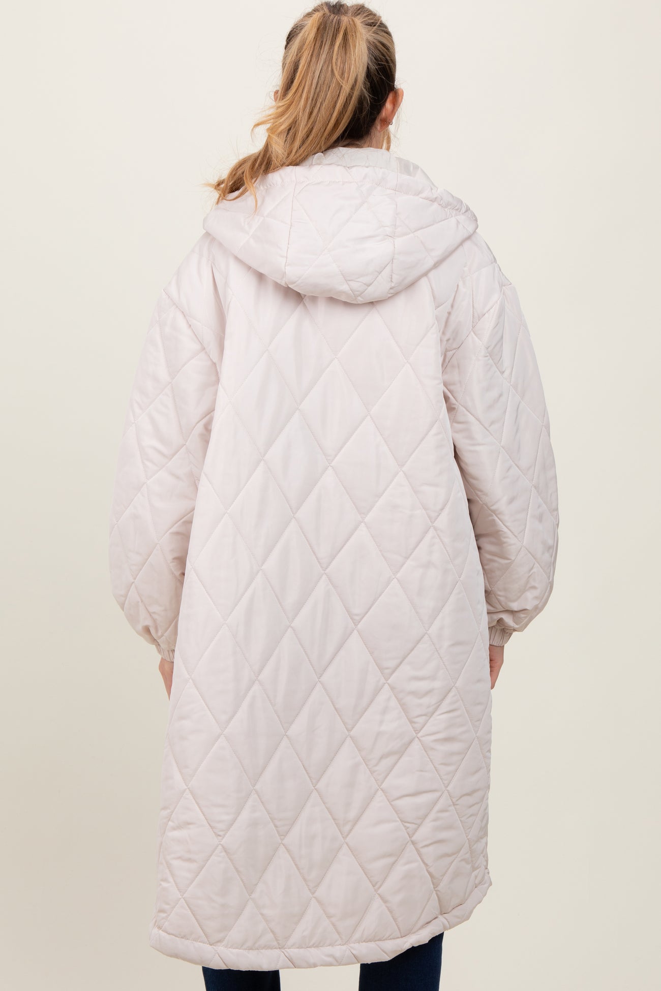 woman wearing a light pink quilted maternity coat with a hood and oversized sleeves, showing the back view