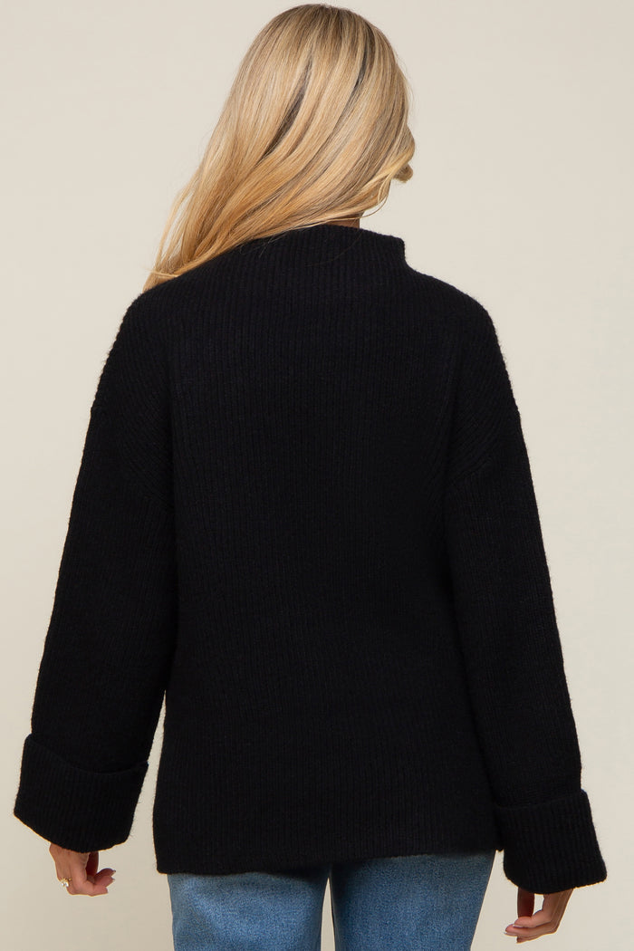 woman wearing a black oversized maternity sweater with a high neck and wide cuffs, viewed from the back
