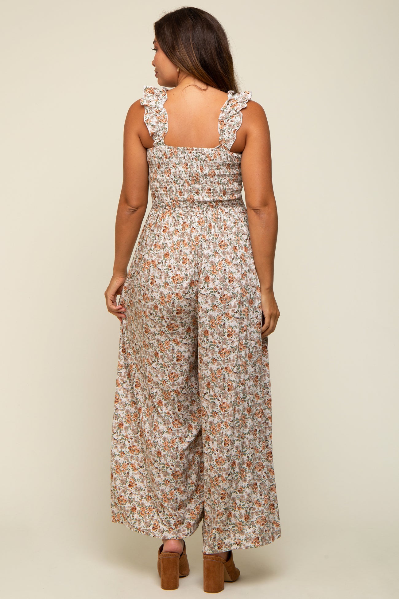 woman wearing a floral maternity jumpsuit with ruffled straps, showing a relaxed fit and wide legs from the back