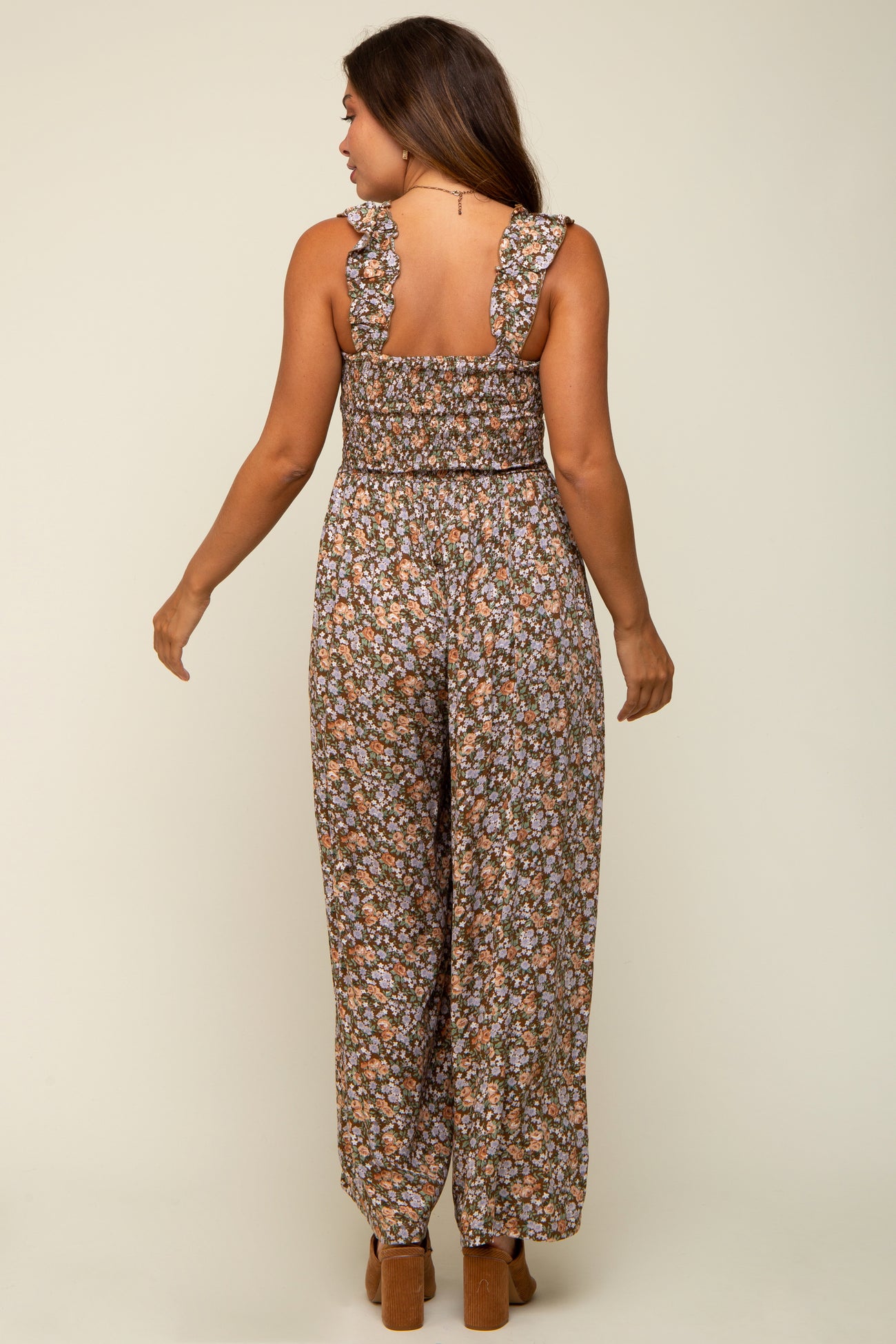 woman wearing a floral maternity jumpsuit with ruffled straps and wide legs, showing her back and a baby bump