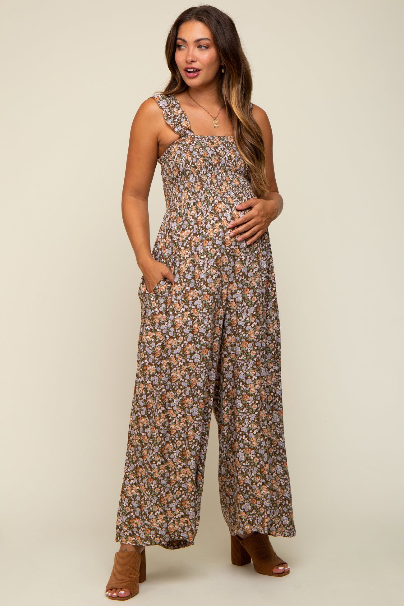 woman wearing a brown floral maternity jumpsuit with pockets, showing her baby bump