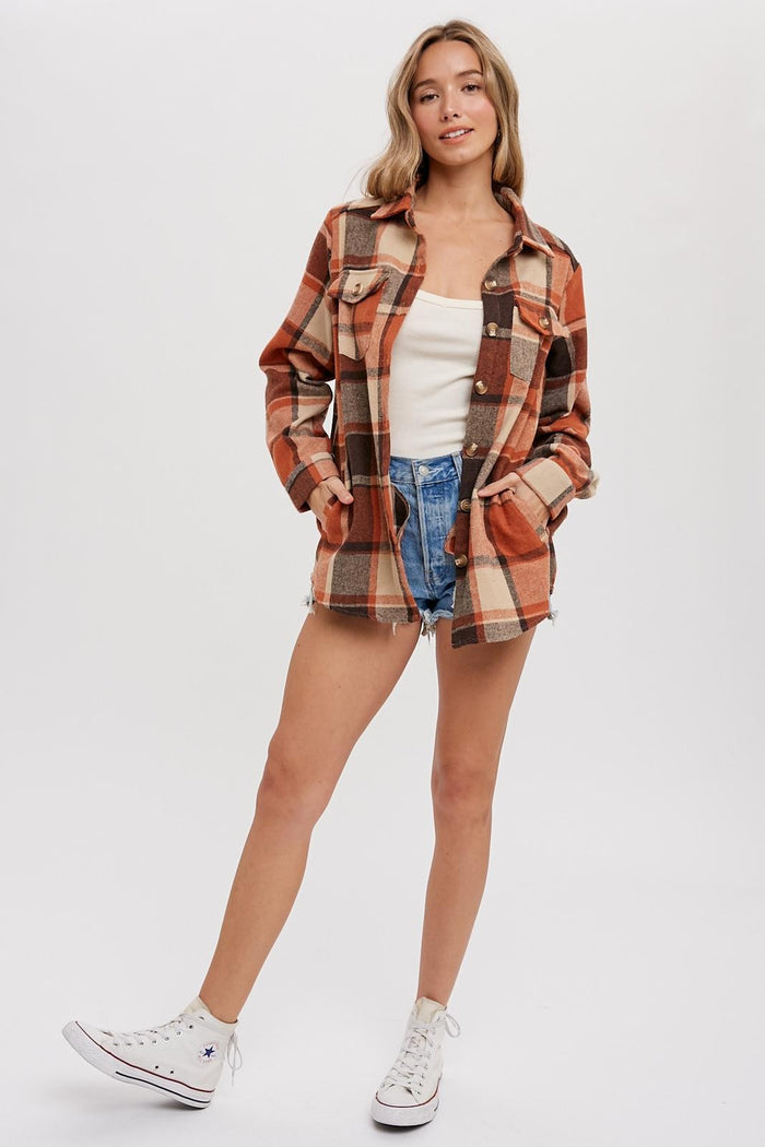 woman wearing an orange and brown plaid shacket over a white top and denim shorts, standing with one leg forward