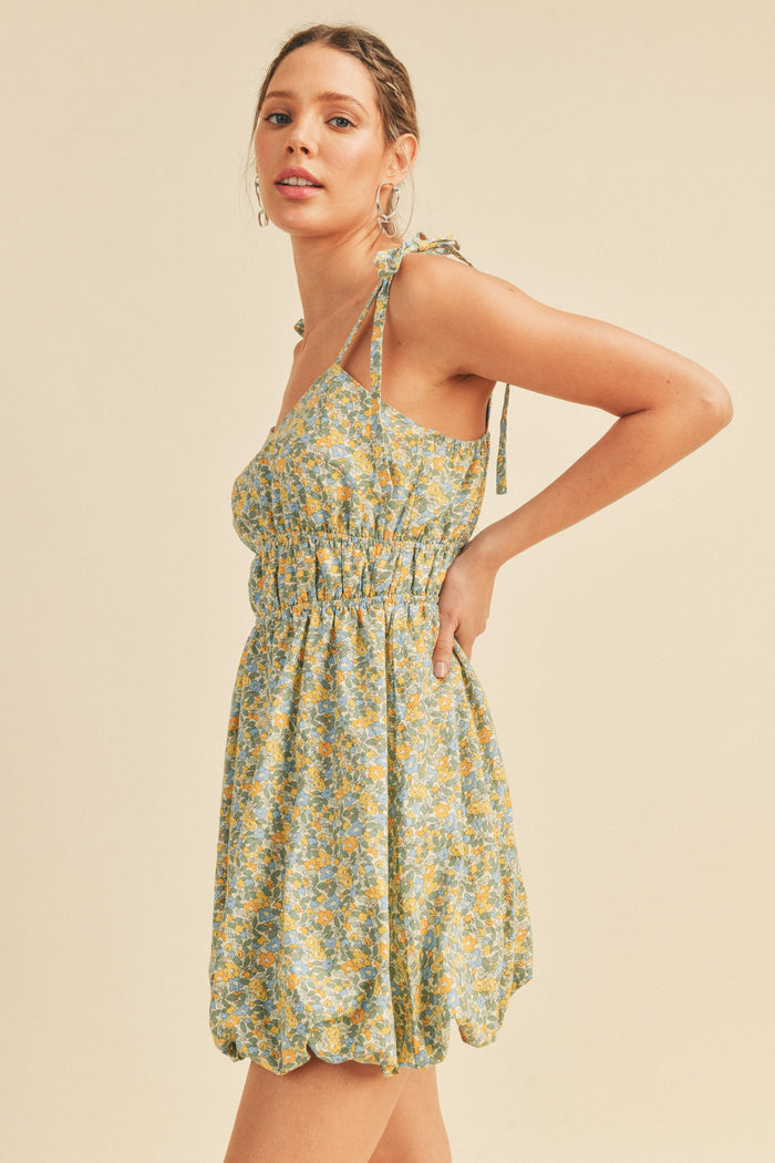 woman wearing a light green floral mini dress with tie straps and a smocked bodice