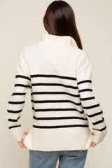 woman wearing a cream and black striped maternity sweater with a high neckline and relaxed fit, showing her baby bump