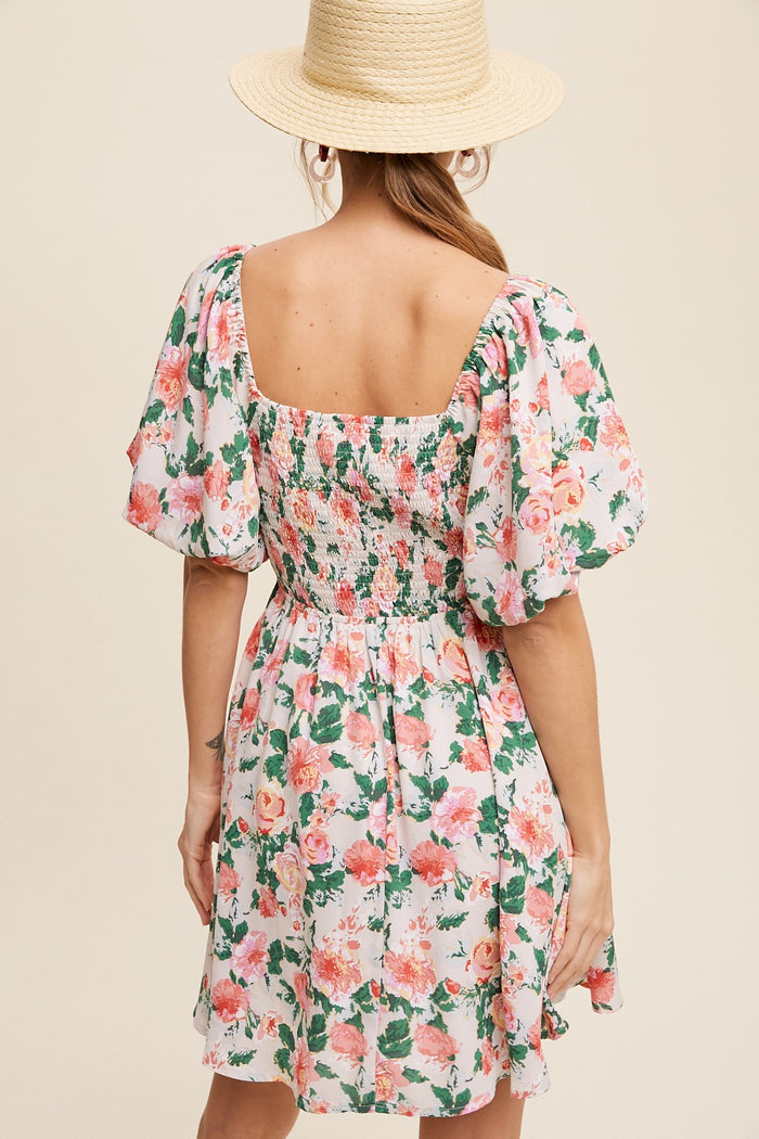 woman wearing a floral short dress with puff sleeves and a smocked back, styled with a straw hat