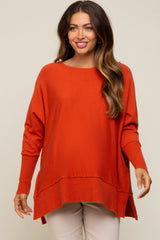 Woman wearing an oversized burnt orange knit sweater with a high-low hem and ribbed cuffs