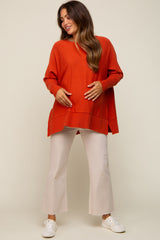 Pregnant woman wearing an oversized orange maternity sweater and cream flare pants with white sneakers