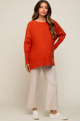 woman wearing an orange oversized maternity sweater and cream flared pants, baby bump visible