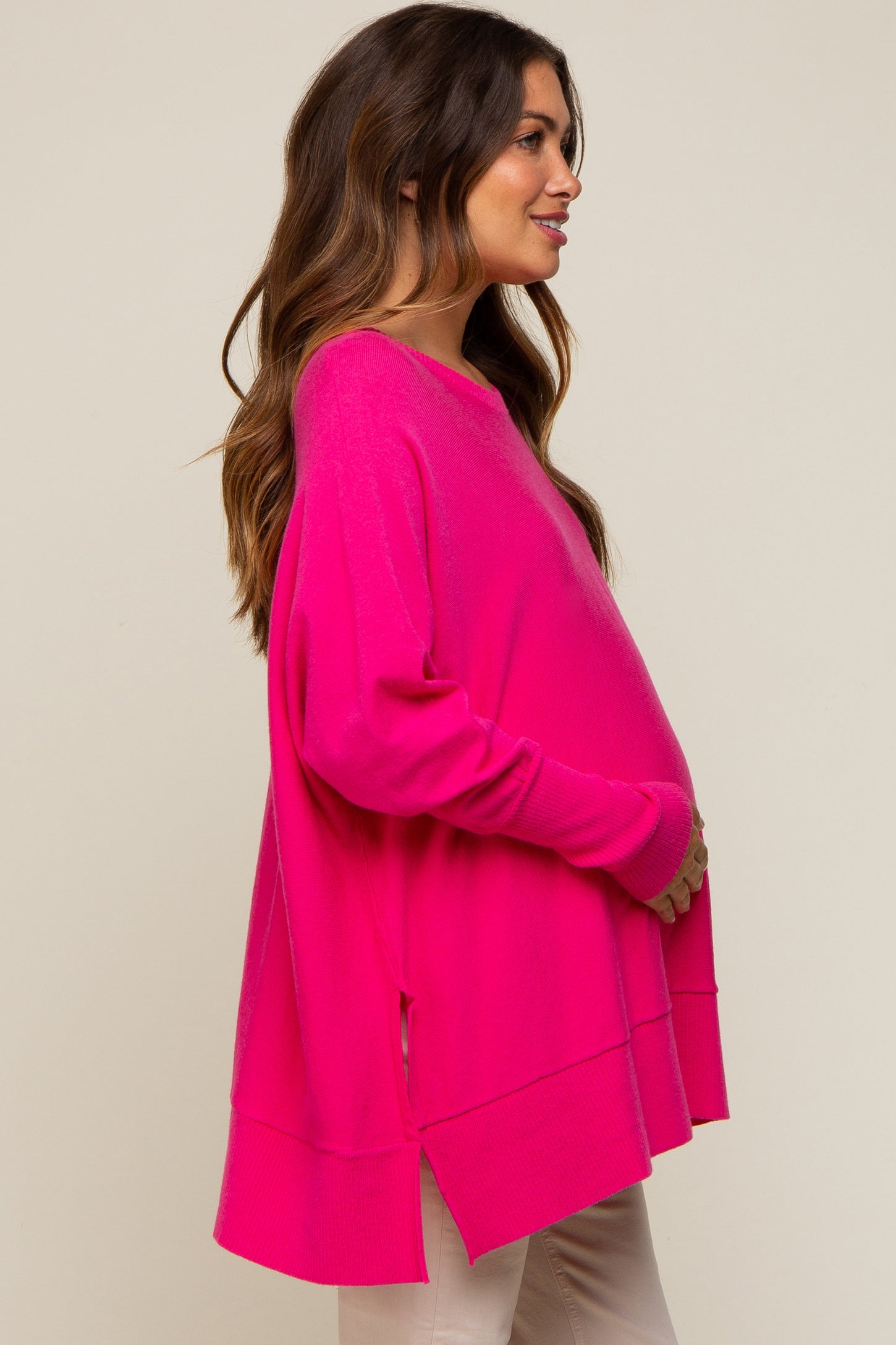 woman wearing a bright pink oversized maternity top with side slits and holding her baby bump