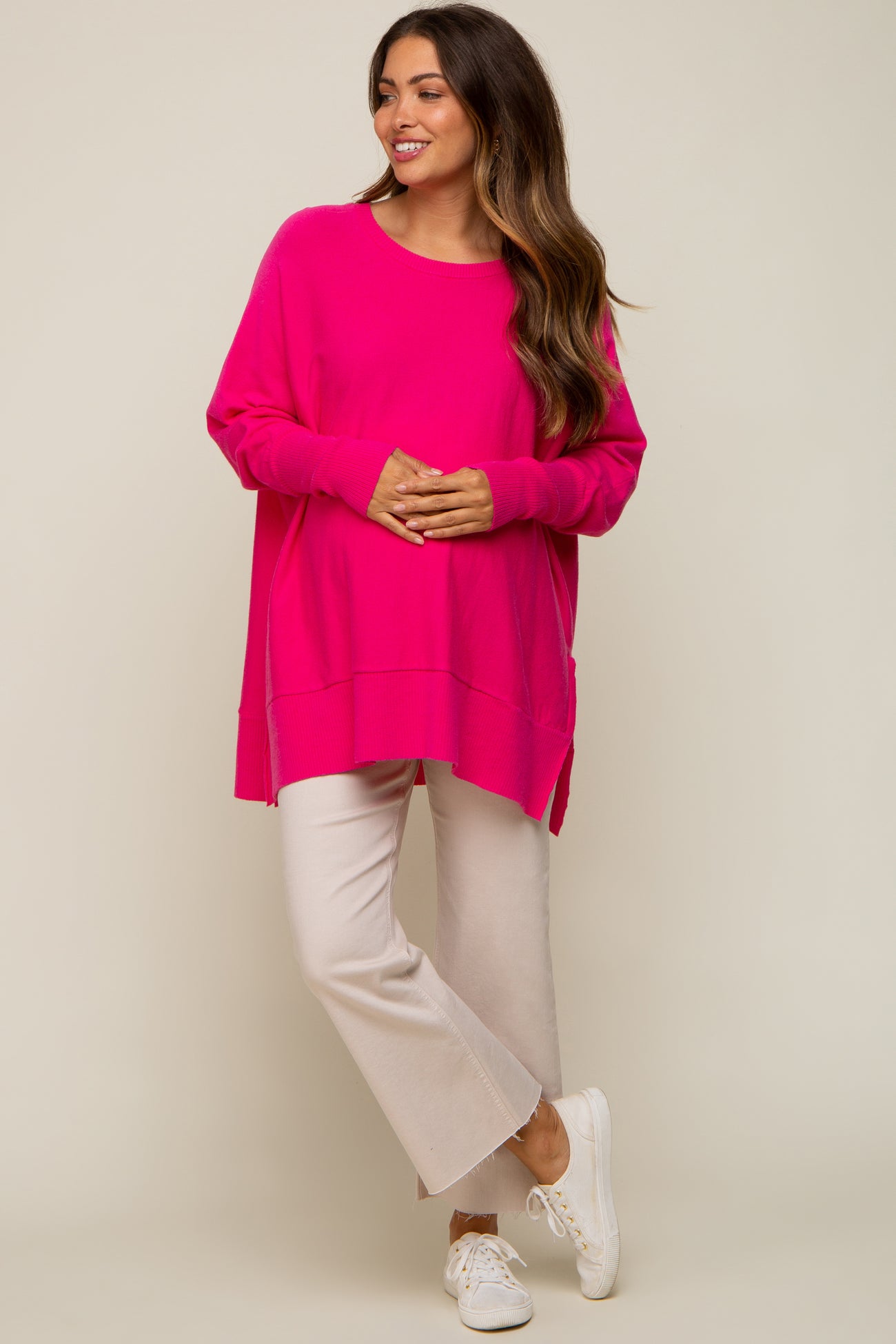 woman wearing a bright pink oversized maternity sweater with side slits and cream-colored cropped pants
