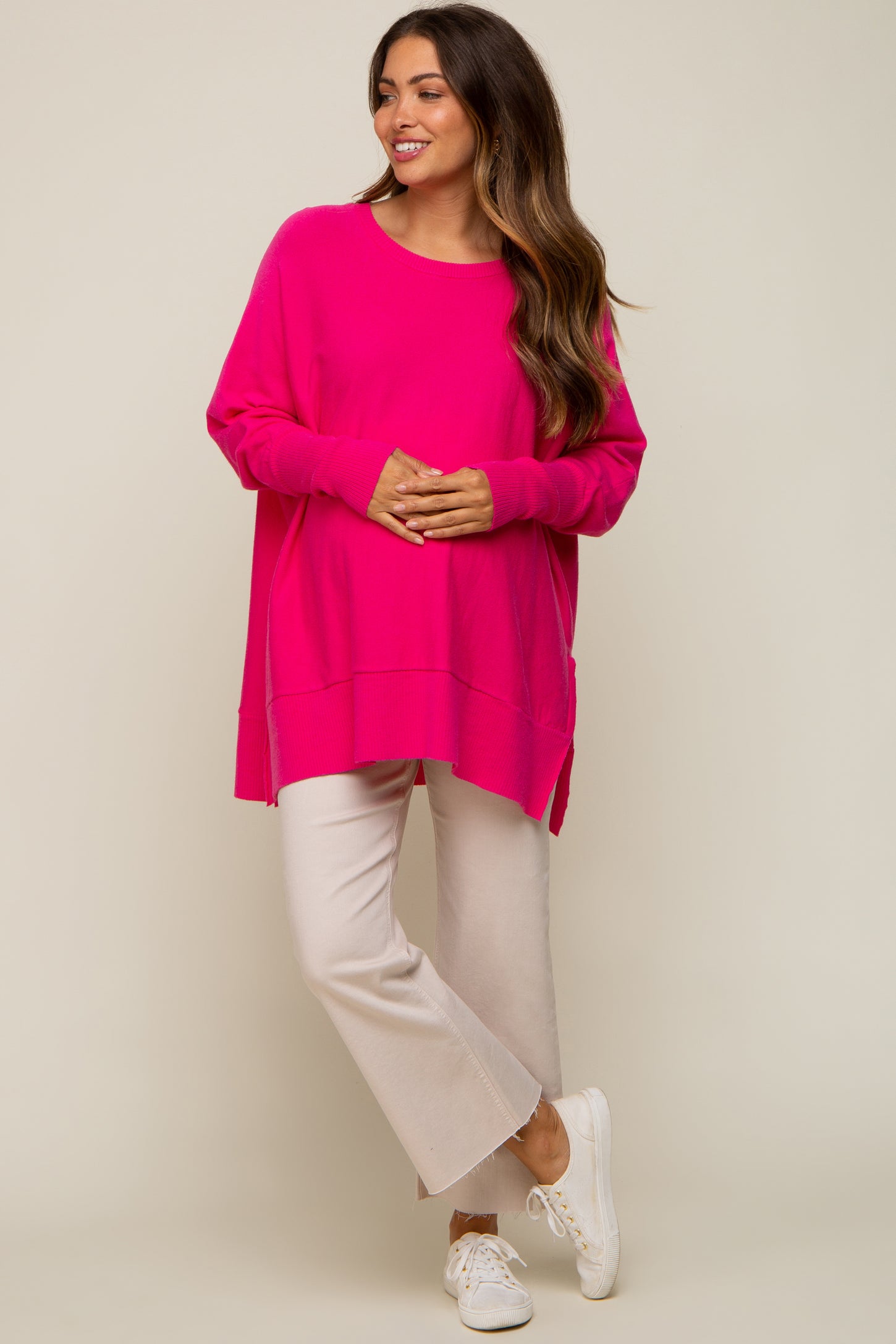 woman wearing a bright pink oversized maternity sweater with side slits and cream-colored cropped pants