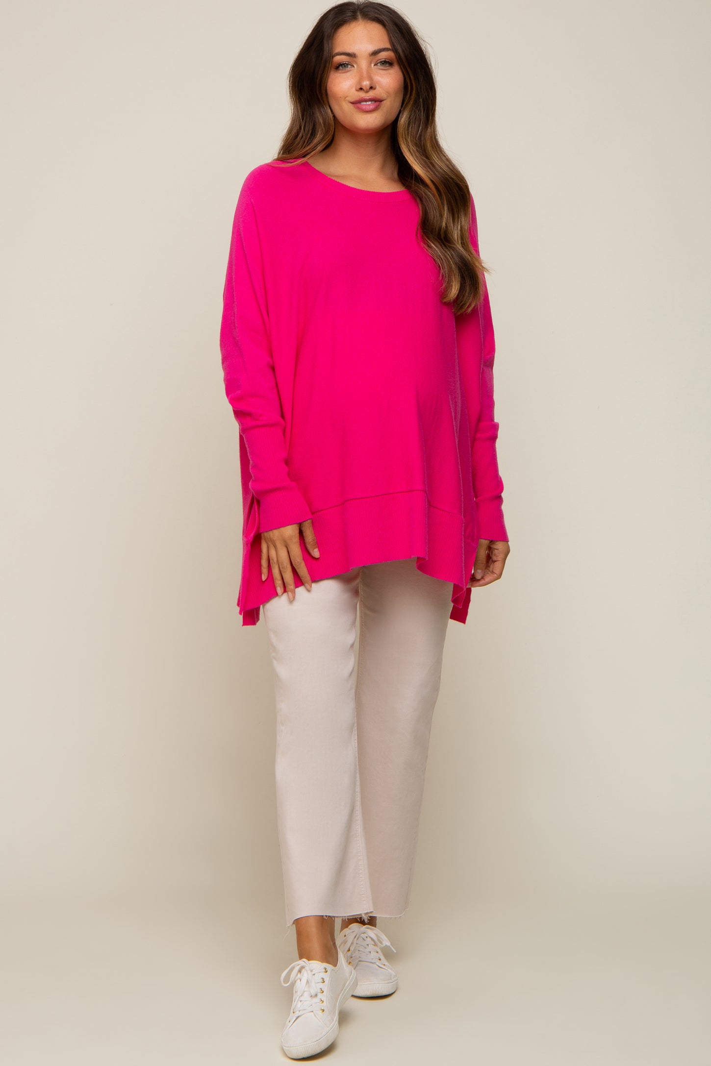 woman wearing a bright pink oversized maternity top and light beige cropped pants, showing her baby bump