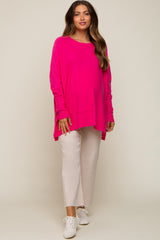 woman wearing a bright pink oversized maternity top and light beige cropped pants, showing her baby bump
