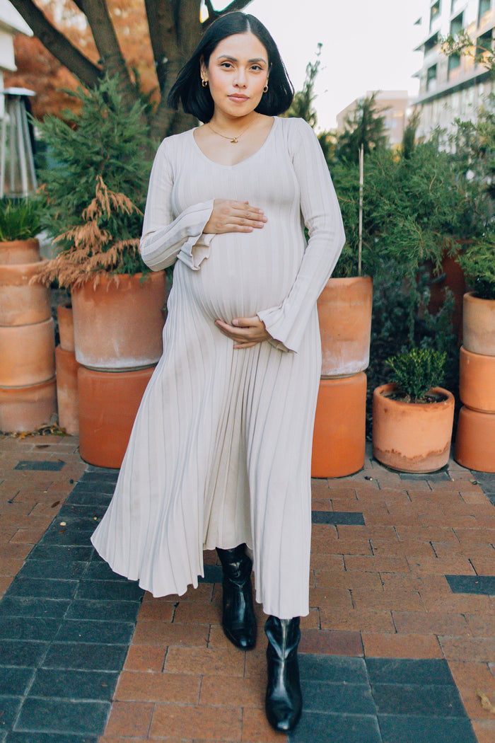 woman wearing a light beige long sleeve maternity dress with flared sleeves and a visible baby bump