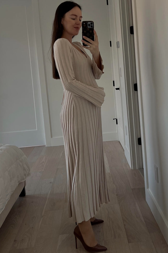 woman wearing a beige ribbed maternity dress and gently holding her baby bump