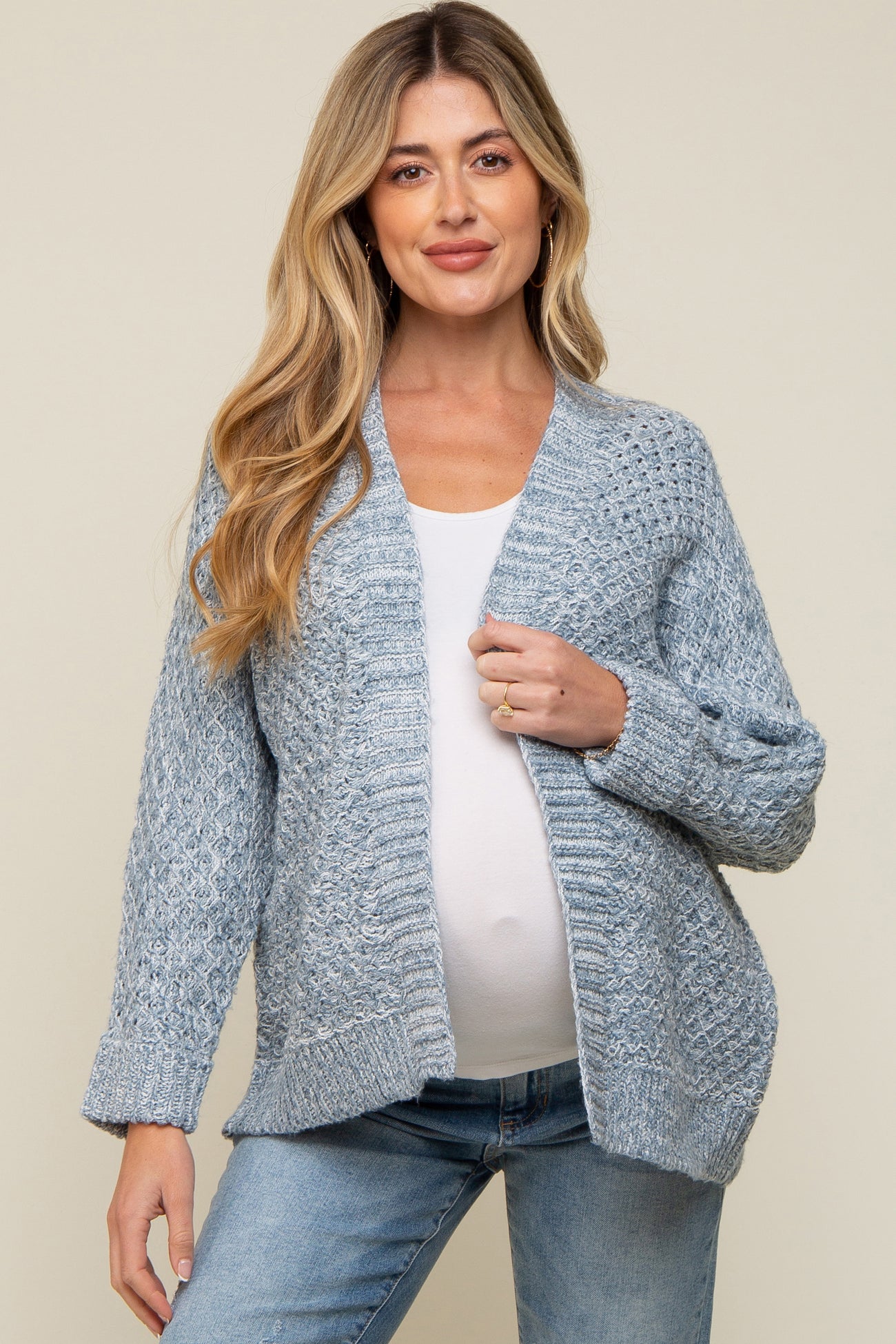 woman wearing a light blue maternity cardigan and a white top, showing her baby bump, paired with blue jeans