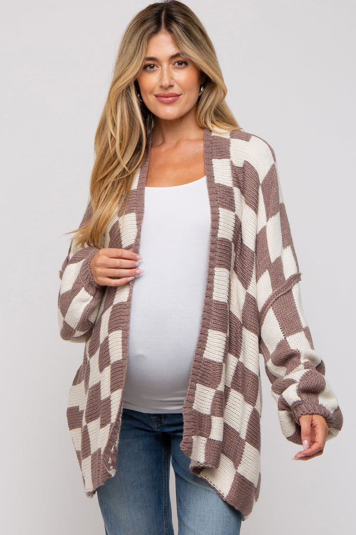 woman wearing a brown and cream checkerboard maternity cardigan over a white top and showing her baby bump