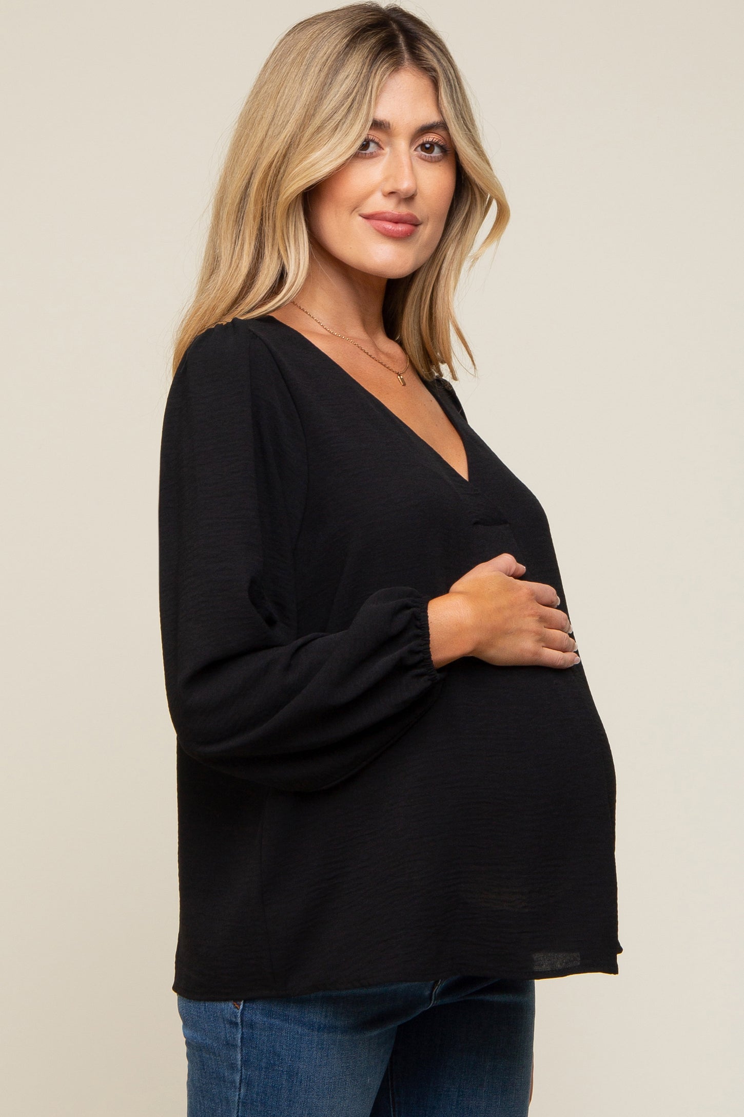 woman wearing a black maternity top with a deep v-neck and long sleeves, holding her baby bump