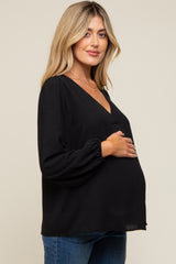 woman wearing a black maternity top with a deep v-neck and long sleeves, holding her baby bump