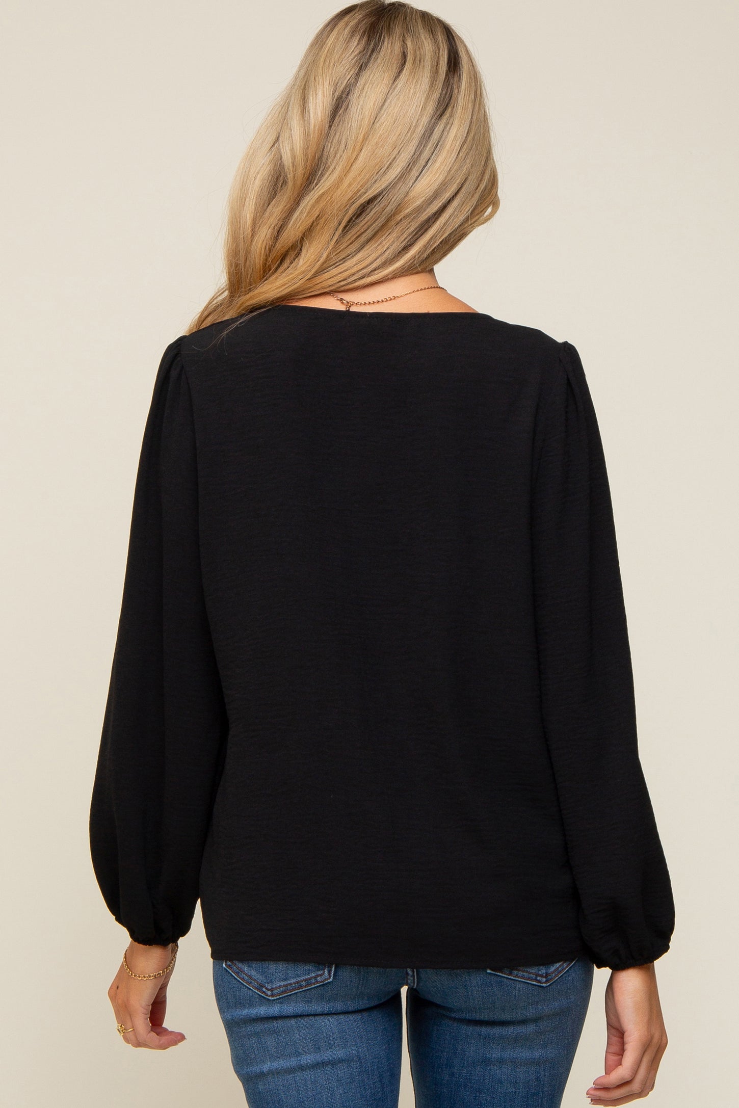 woman wearing a black long sleeve maternity top viewed from the back, styled with puff sleeves and a relaxed fit