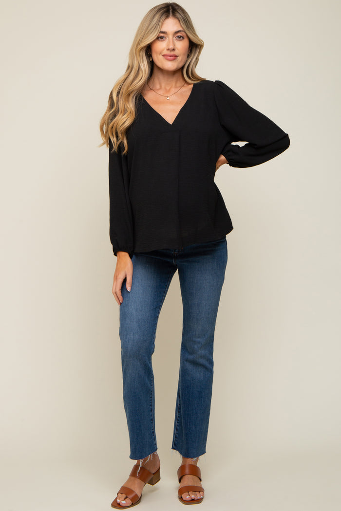 woman wearing a black maternity top with a v-neck and puff sleeves, paired with blue jeans and brown sandals