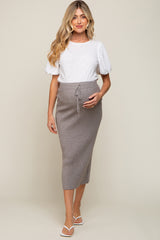woman wearing a white short sleeve top and a gray ribbed maternity skirt, showcasing her baby bump