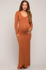 woman wearing a rust long sleeve maternity maxi dress and holding her baby bump